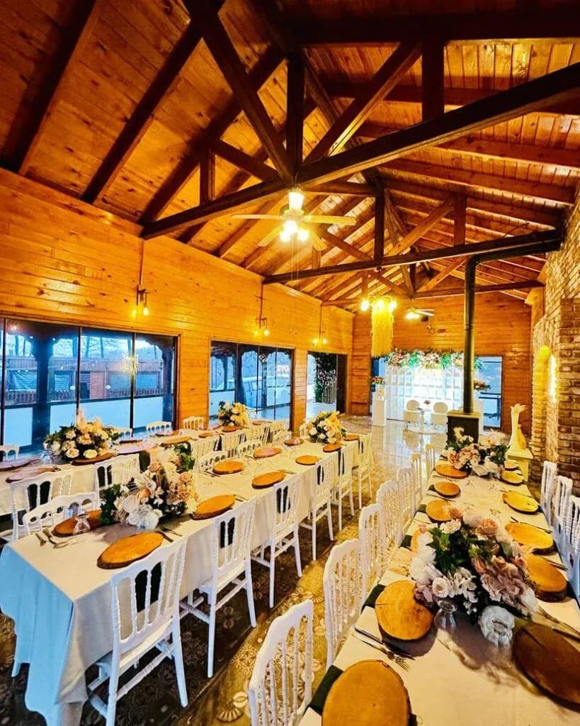 Ahşap tavanlı kapalı salon, uzun masalar ve çiçek süslemeleri